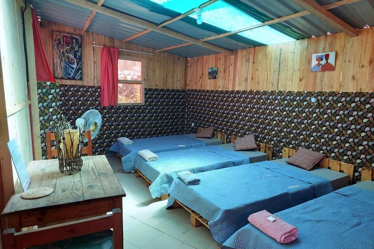 A room with three beds, a wooden table, and a fan.
