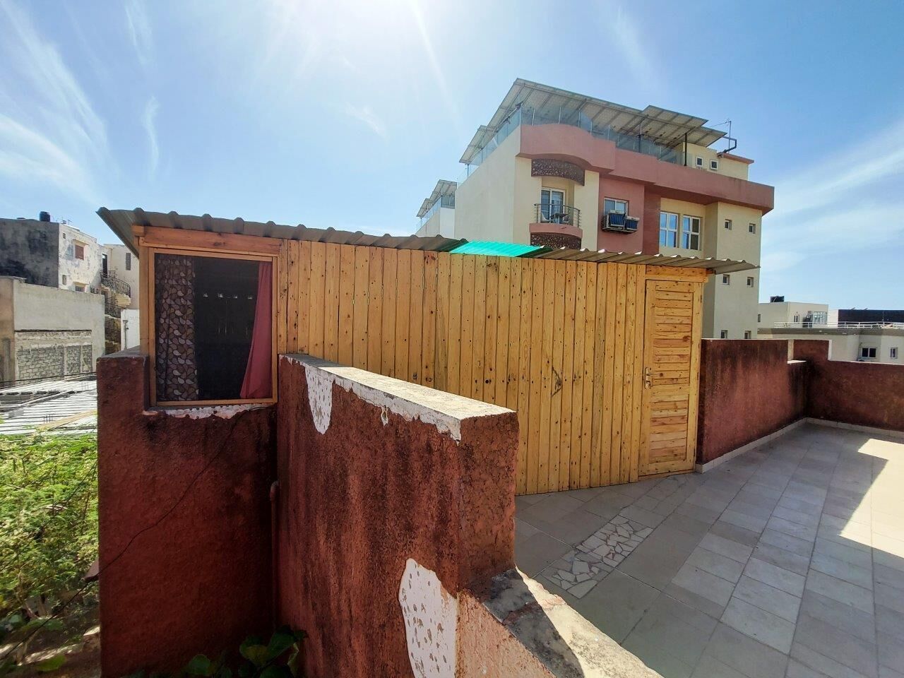 Un edificio residencial con cerca de madera, balcón y zona de patio con baldosas.