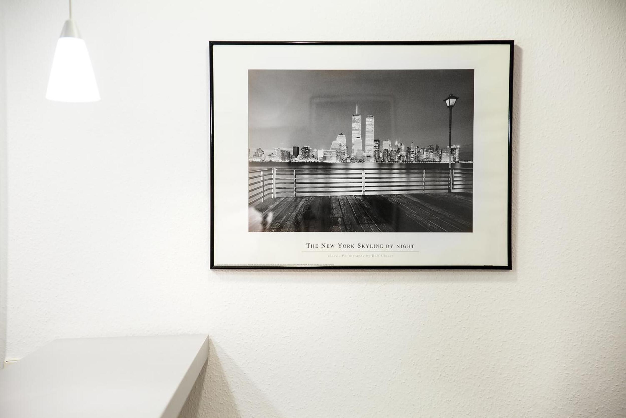 Fotografía enmarcada del horizonte de Nueva York de noche, montada sobre una pared blanca.
