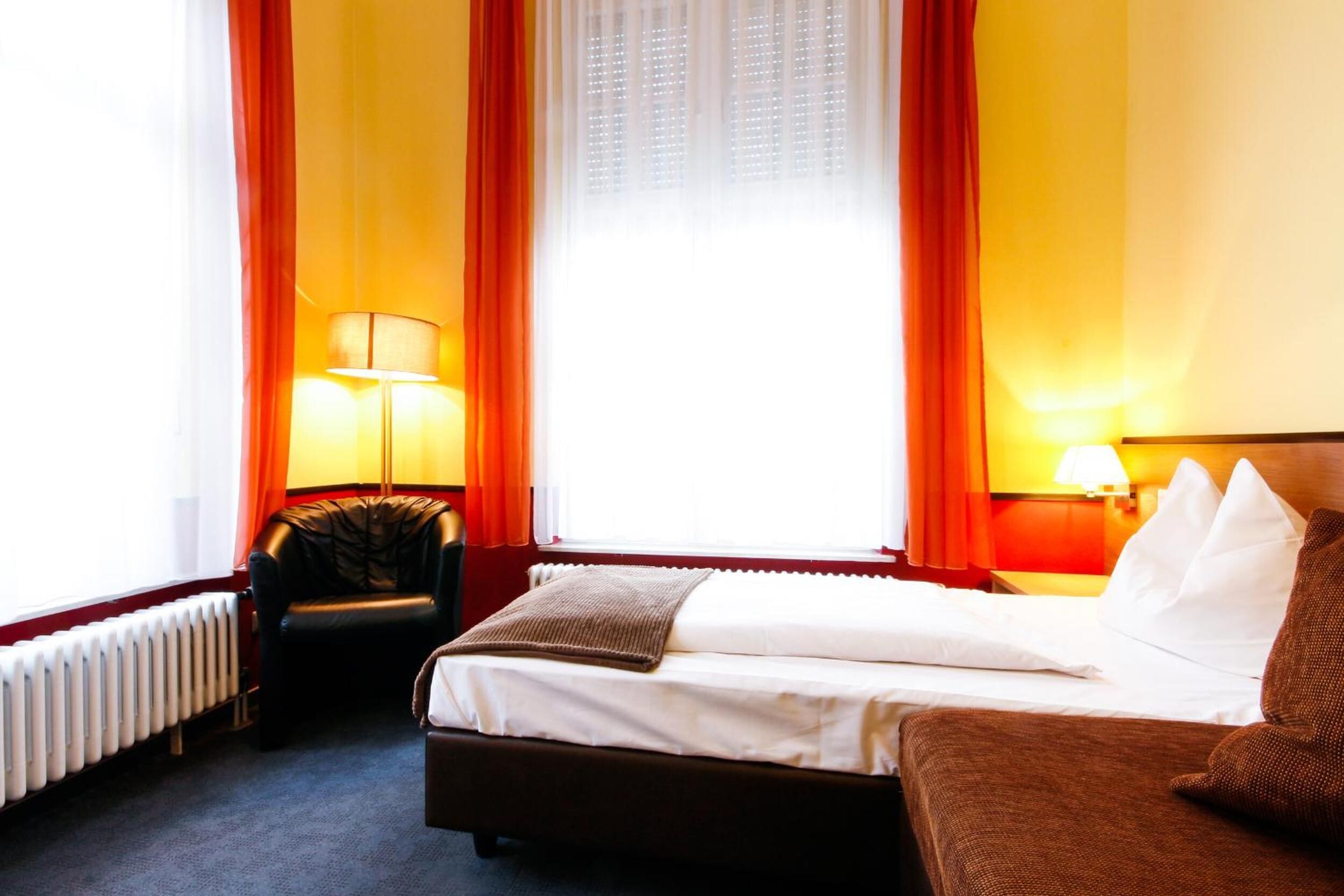 A hotel room with a bed, a chair, a lamp, and a window with curtains.