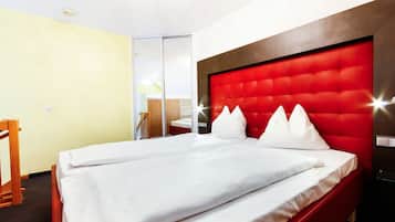 Habitación de hotel con cama, una silla de madera, cabecera roja y una puerta corredera que da al baño.