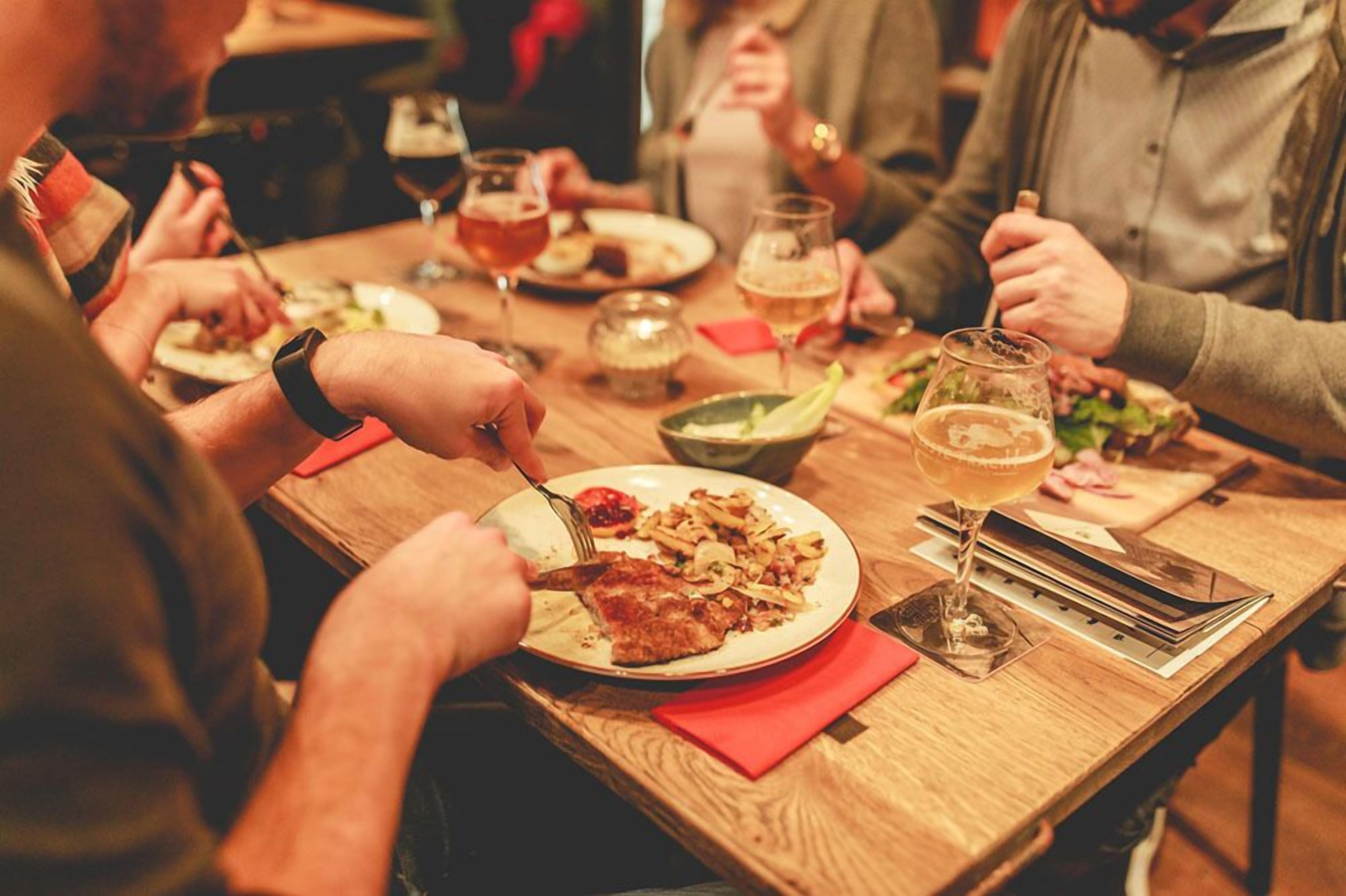 A wooden dining table with plates of food, glasses of beer, and a red napkin.