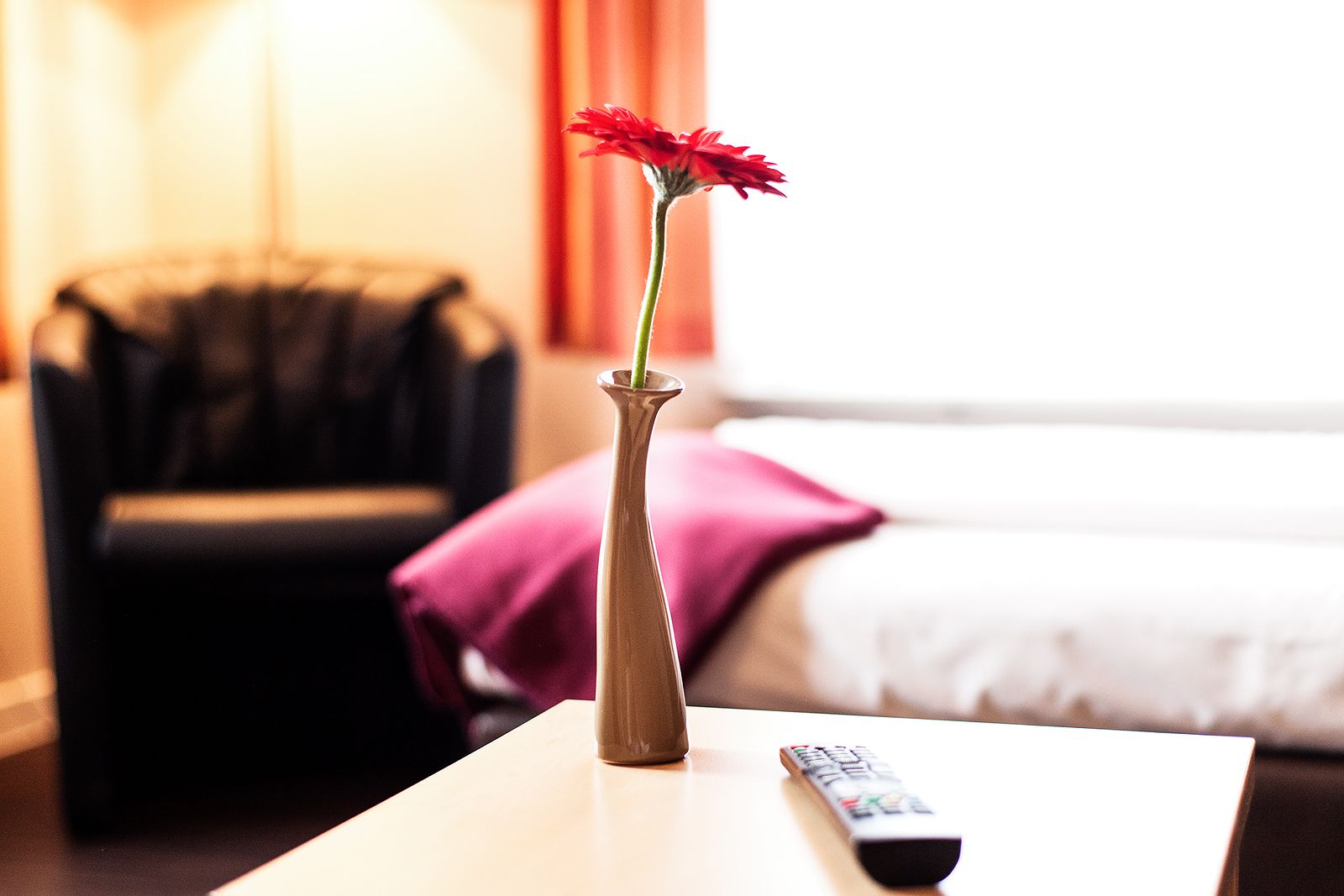 A vase with a single red flower on a table in a hotel room.