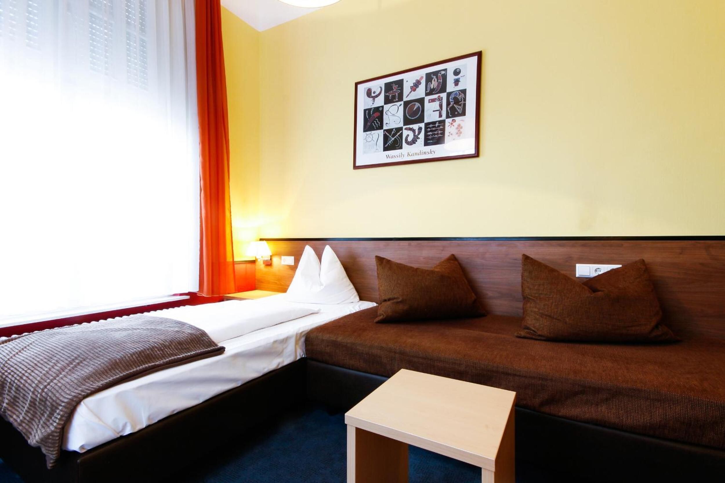 A hotel room with a bed, a sofa, a small table, and a framed artwork on the wall.