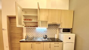 A compact kitchen with light wooden cabinets, a stainless steel sink, a microwave, and a small refrigerator.