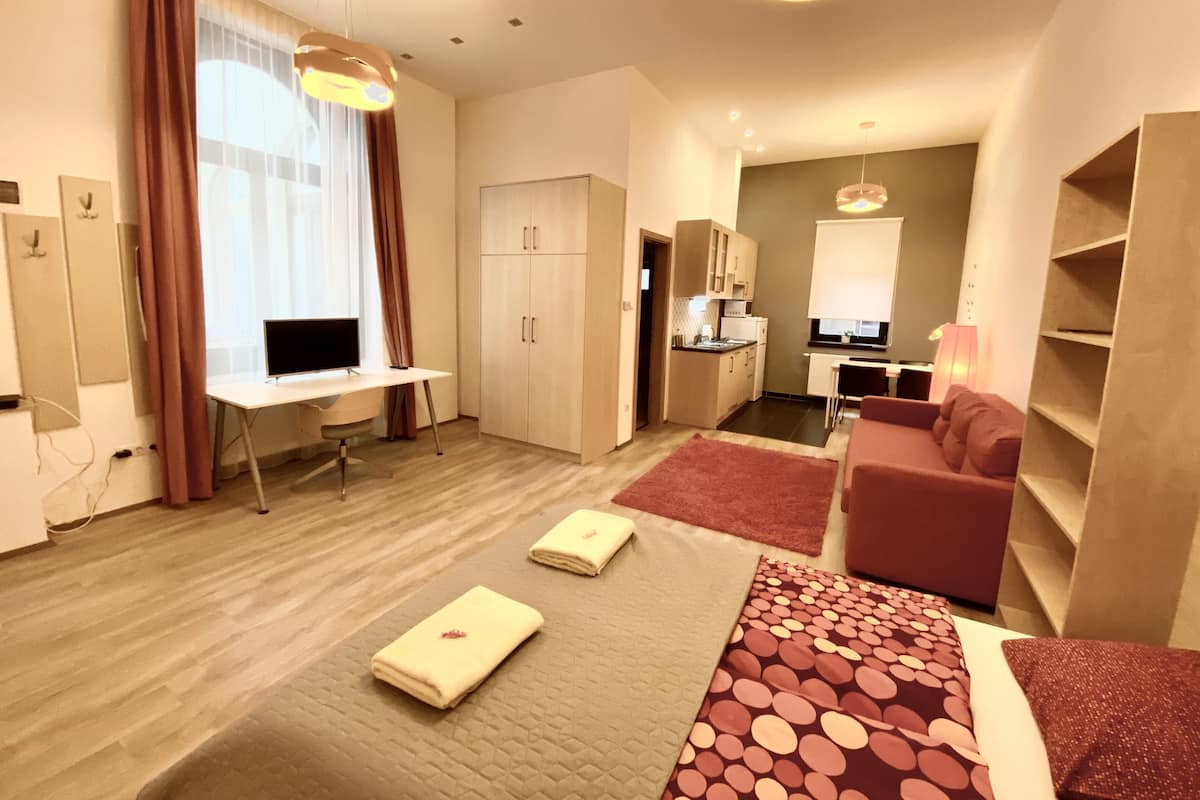 A modern hotel room with a desk, kitchenette, and a cozy seating area.