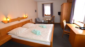 A hotel room with a wooden bed, a desk, a chair, a small table, and a television. - Pension Weidemühle (Kelbra)