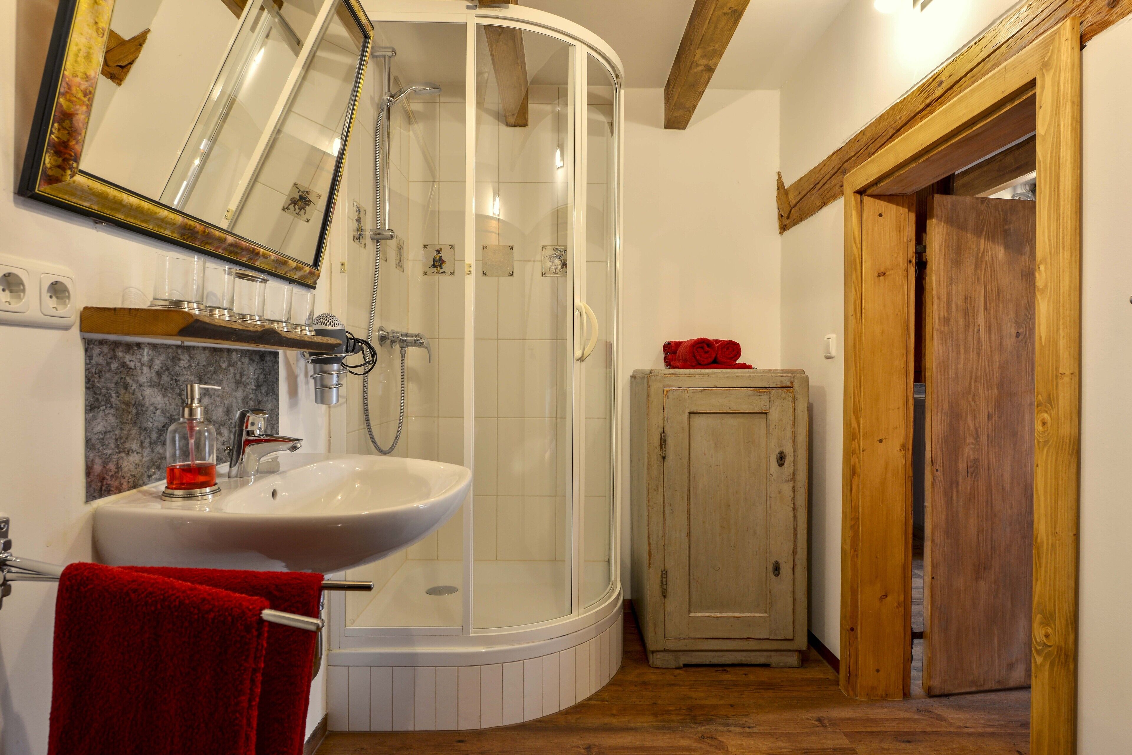A bathroom with a shower, sink, and wooden cabinet.