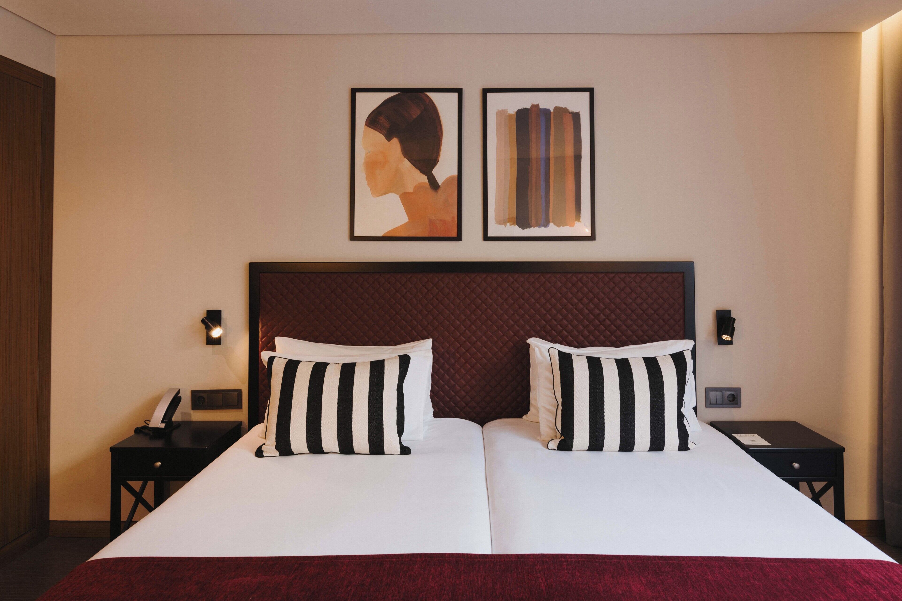 A hotel room with a large bed, two bedside tables, a telephone, and two framed artworks on the wall.