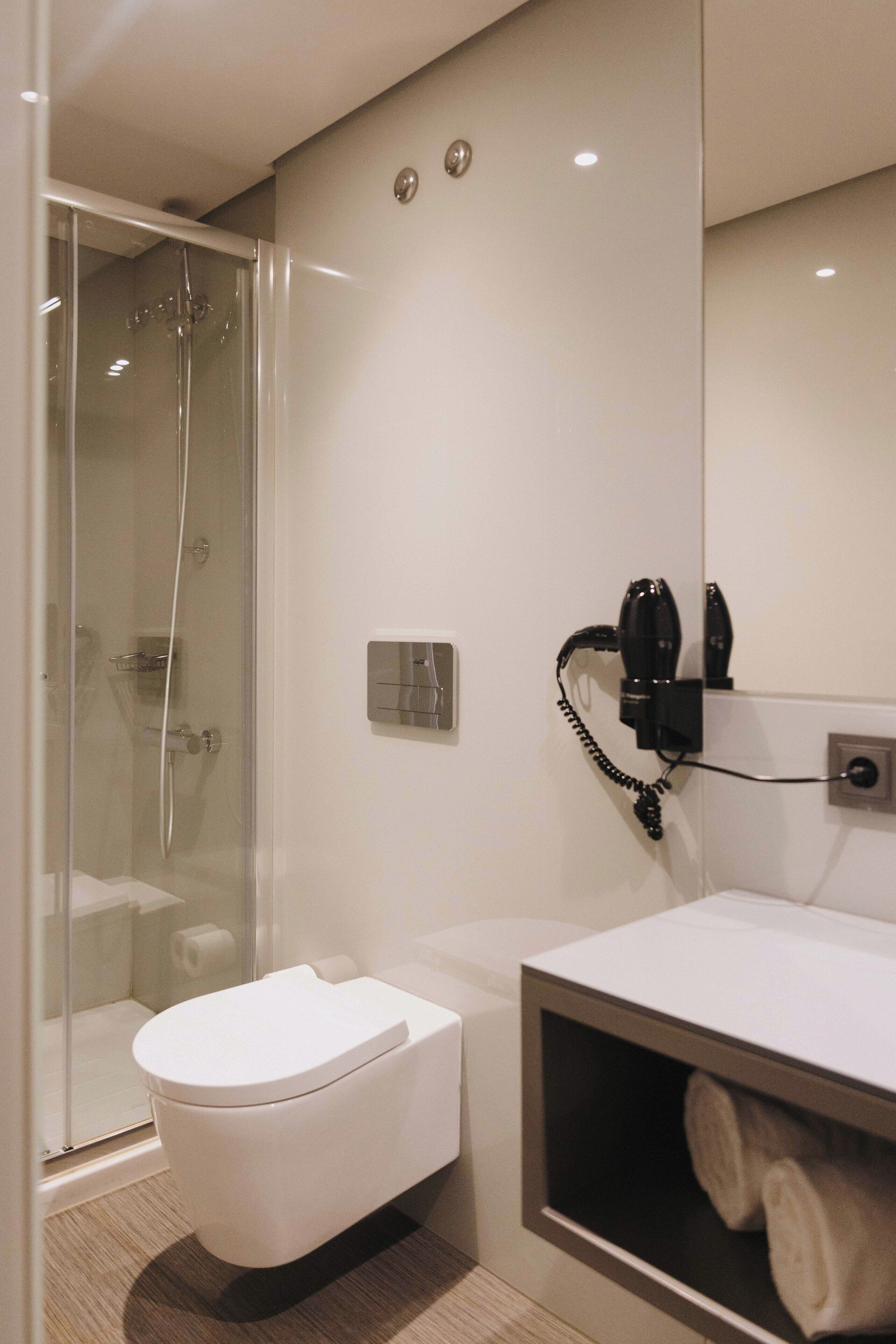 Et moderne badeværelse med brusekabine i glas, et hvidt toilet og en håndklædestang.