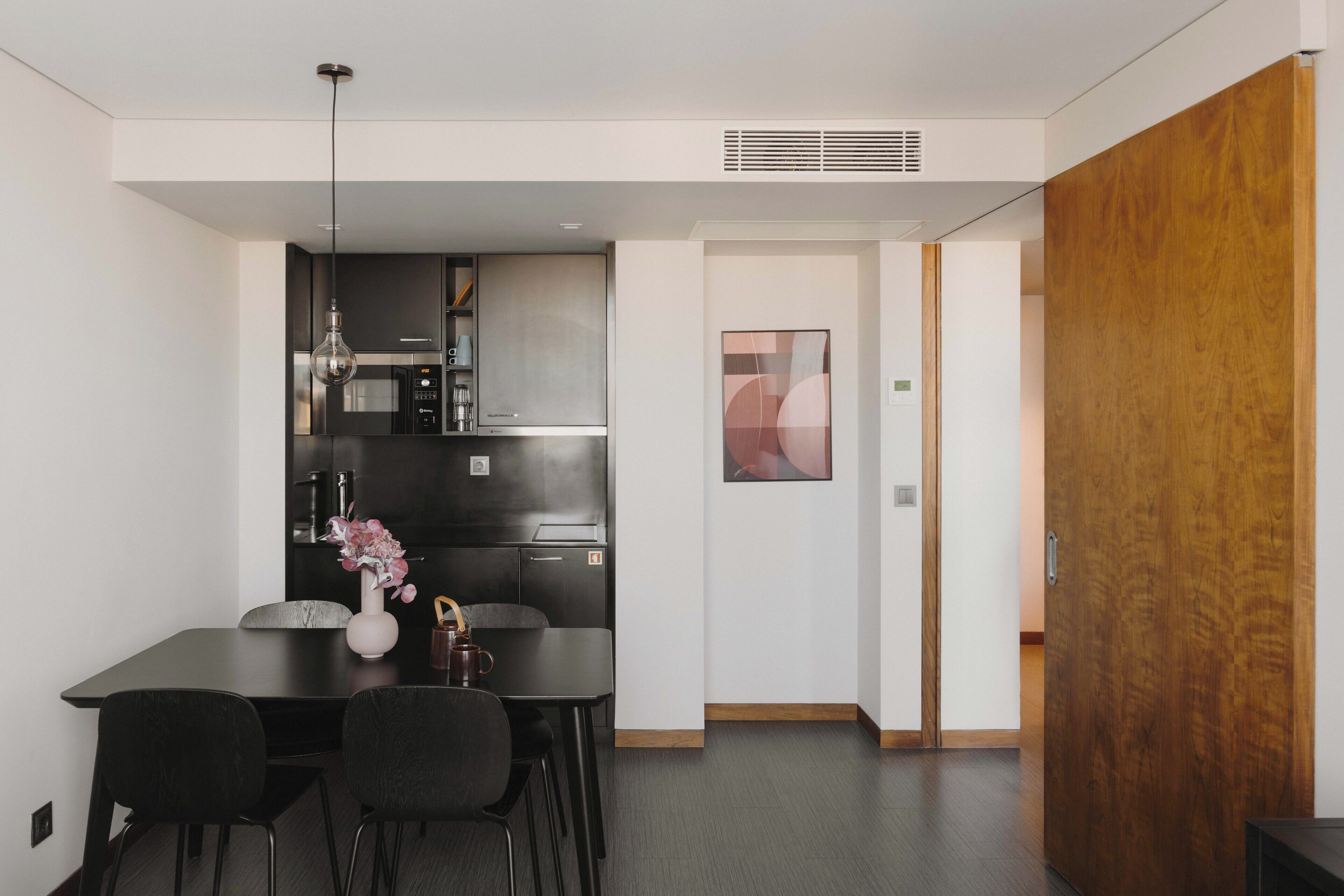 A modern kitchen with dark cabinetry, a dining table with chairs, and a vase with flowers.