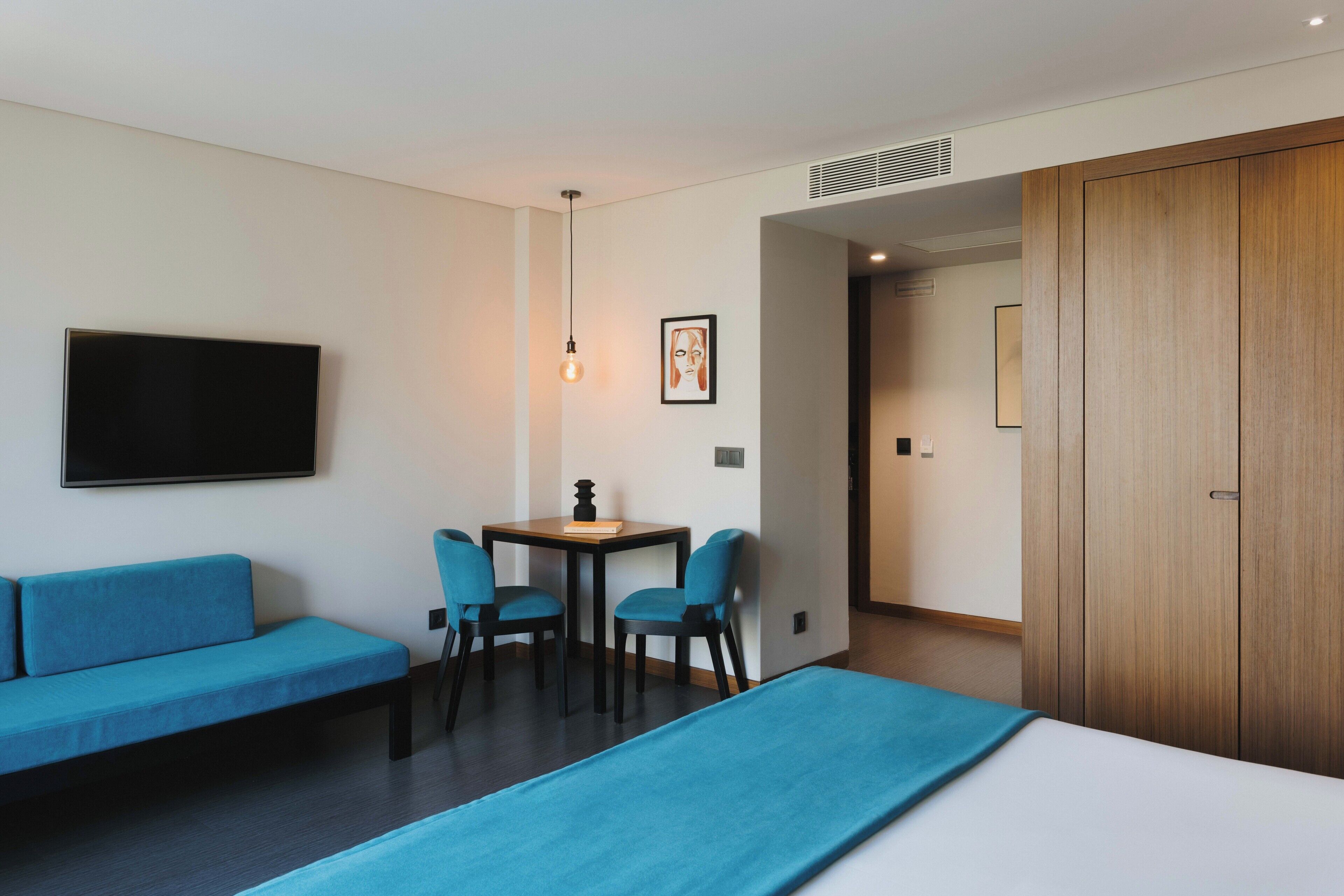 Ein Hotelzimmer mit einem Bett, einem blauen Sofa, einem kleinen Tisch mit Stühlen, einem Fernseher und einem Holzschrank.