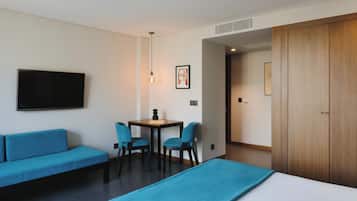 Ein Hotelzimmer mit einem Bett, einem blauen Sofa, einem kleinen Tisch mit Stühlen, einem Fernseher und einem Holzschrank.