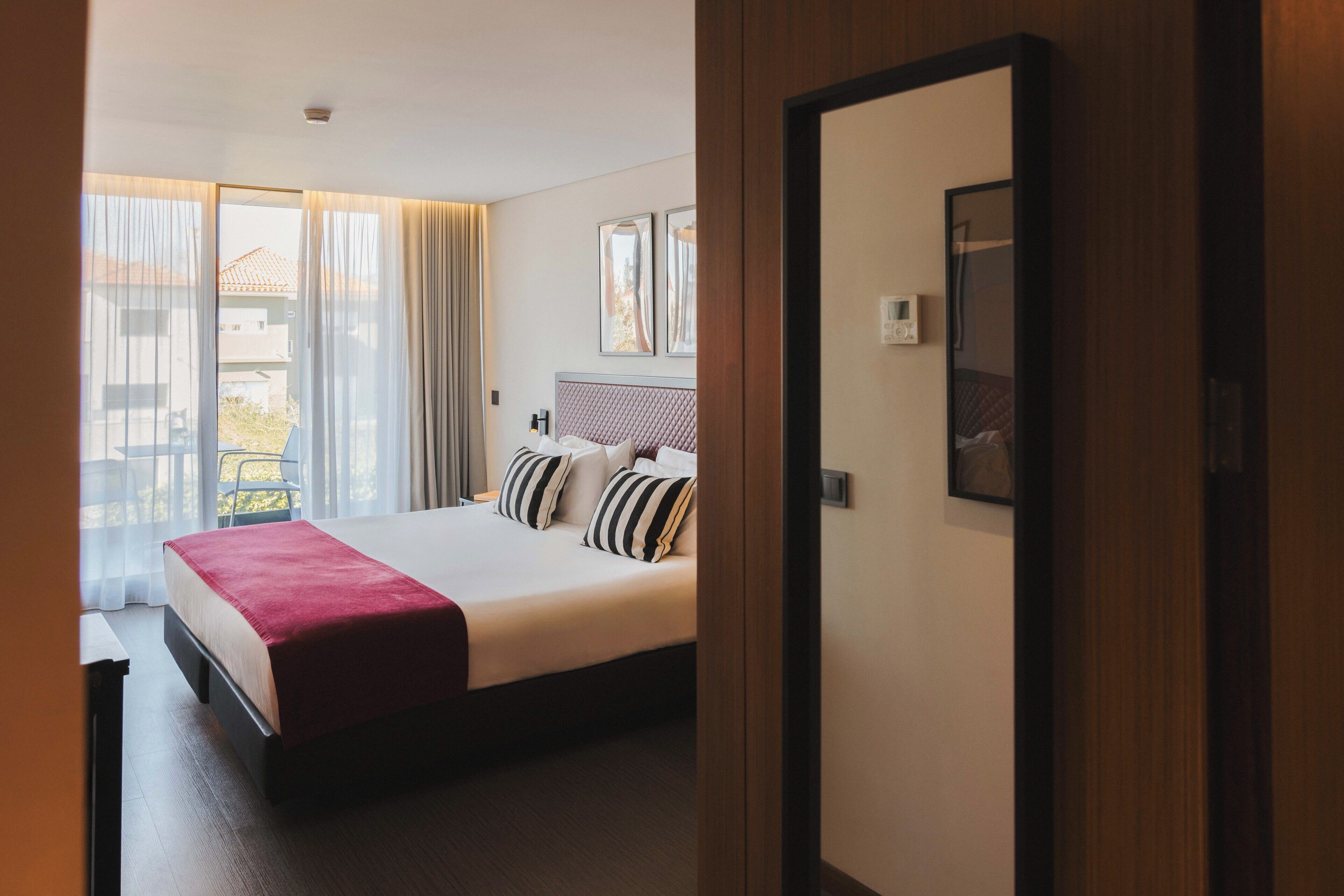 Hotelkamer met een groot bed, uitzicht op het omliggende landschap door een schuifdeur en een lijst met een foto aan de muur.