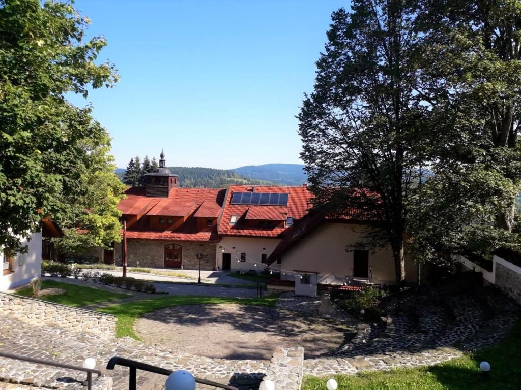 Un bâtiment avec un toit rouge, une cour en pierre et une vue sur des collines lointaines.