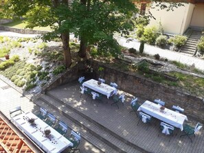 Ein Essbereich im Freien mit Tischen und Stühlen, umgeben von einer Steinmauer und Pflanzen.