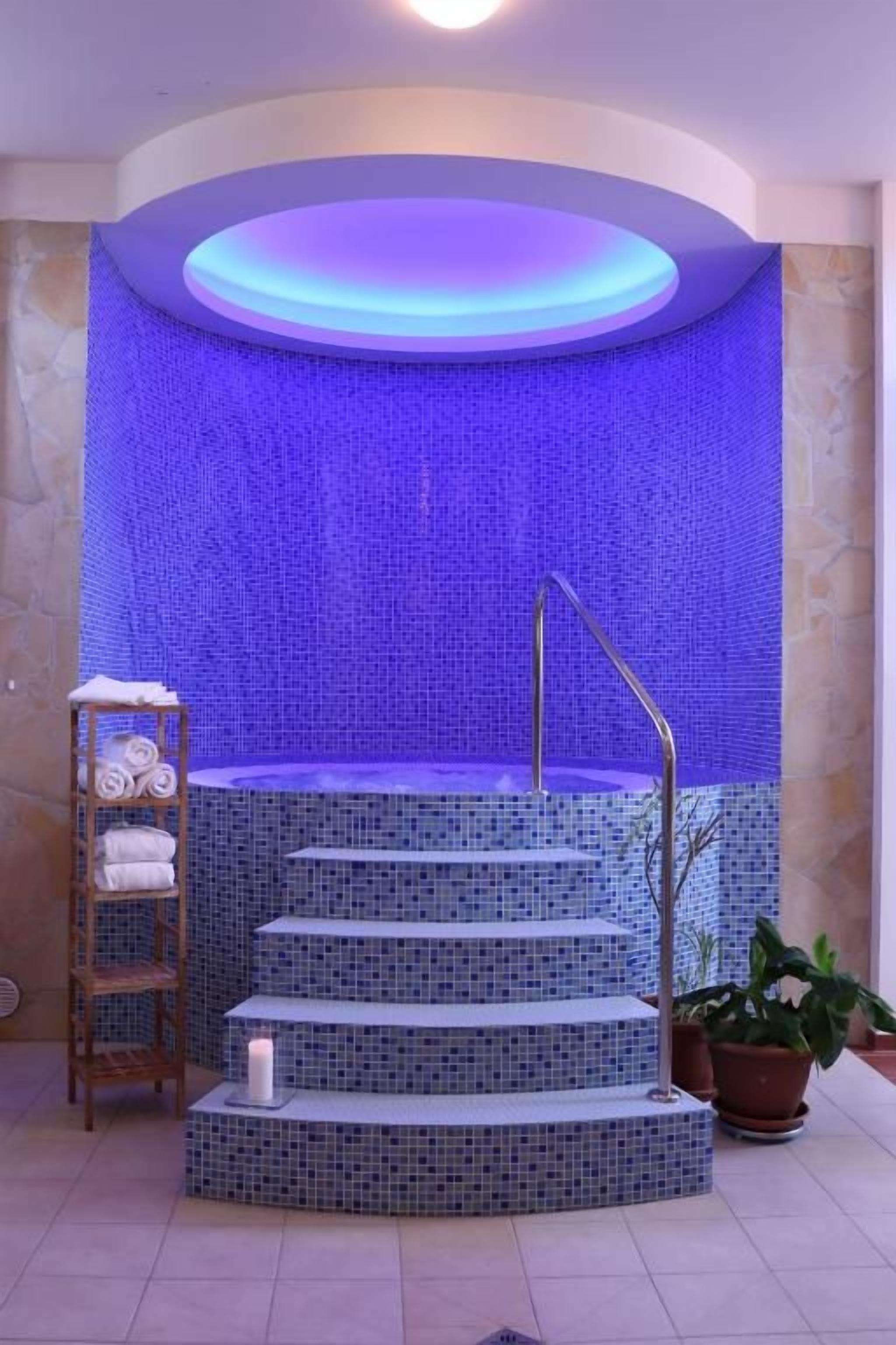 A spa area with a blue-tiled wall, a set of stairs leading to a hot tub, and a shelf with towels.