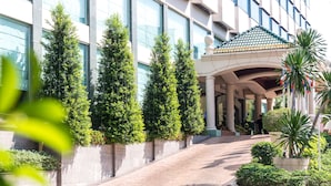 A hotel entrance with a covered walkway, a palm tree, and a building with large windows and a tiled roof.