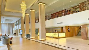 A spacious lobby with a reception desk, large pillars, and a staircase leading to an upper level.