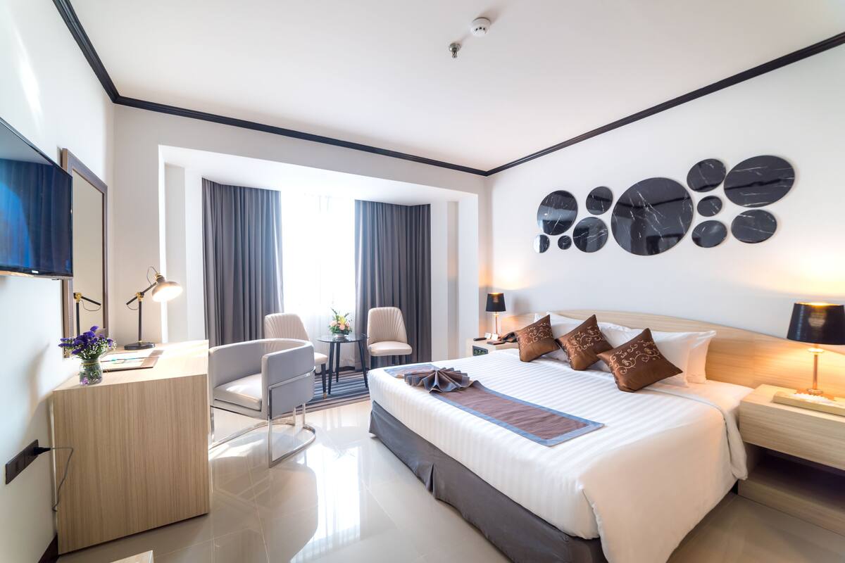 A modern hotel room with a large bed, a desk, a chair, and a TV.