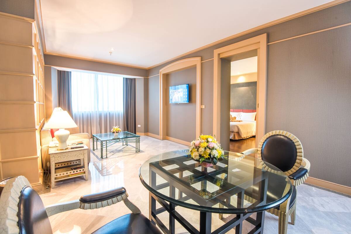 A hotel room with a glass dining table, a sofa, a TV, and a bed.