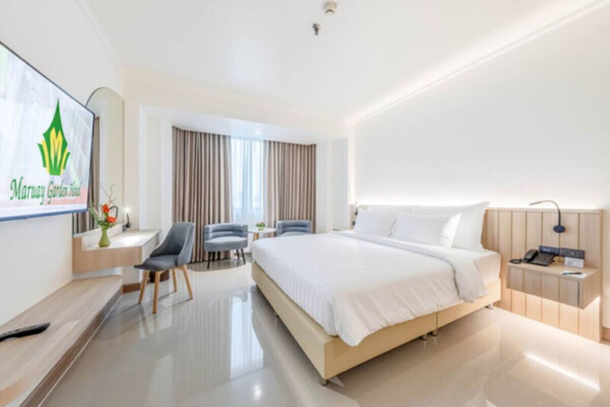 A hotel room with a large bed, a desk with a chair, a small table, and a TV.