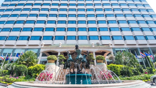 A hotel with a large, modern facade, a central fountain with statues, and multiple flags.