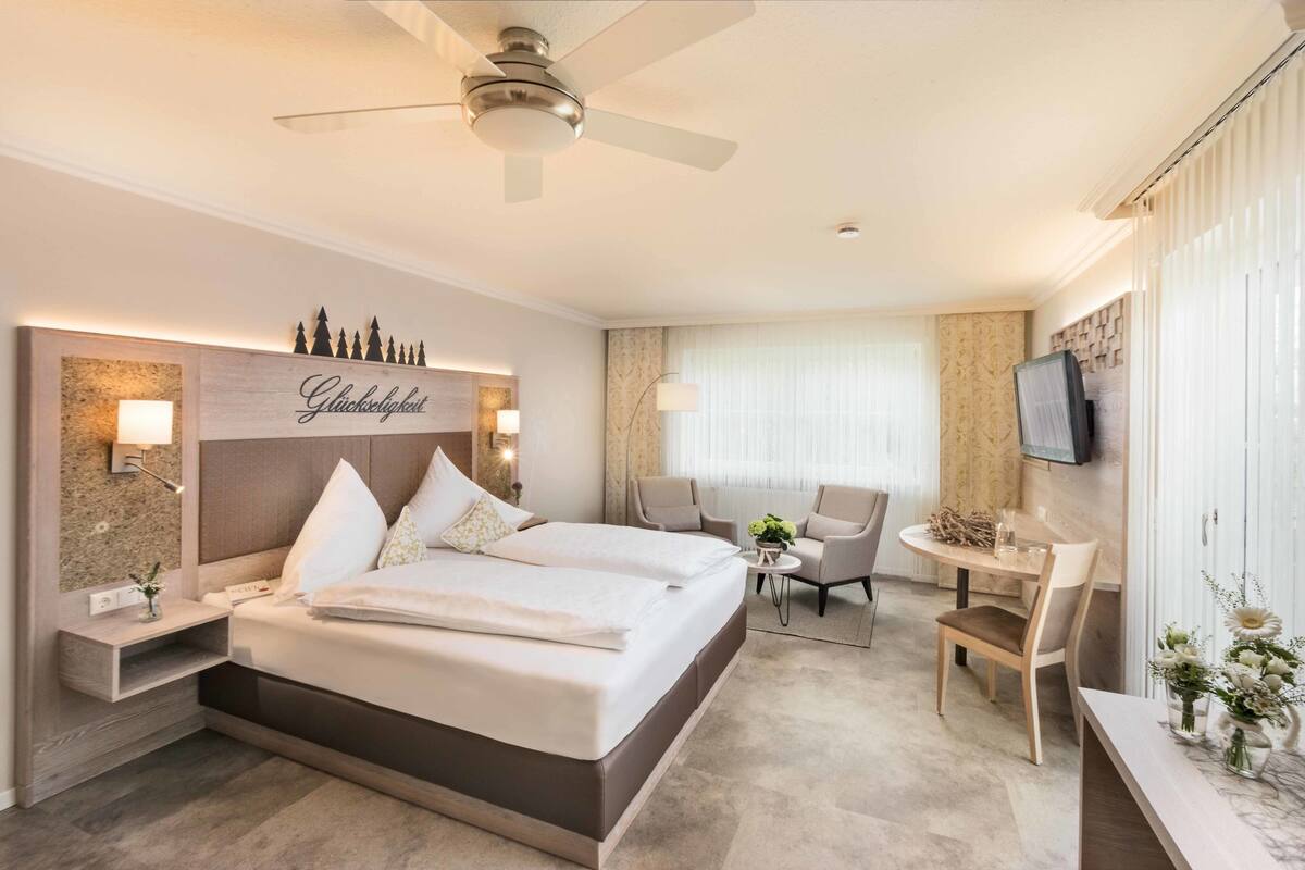 Ein Hotelzimmer mit einem großen Bett, einem Schreibtisch, einem Stuhl, einem Fernseher und einem Deckenventilator.