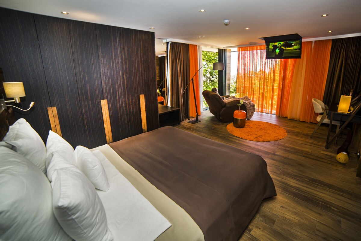 A modern hotel room with a large bed, a desk, a chair, and a TV.
