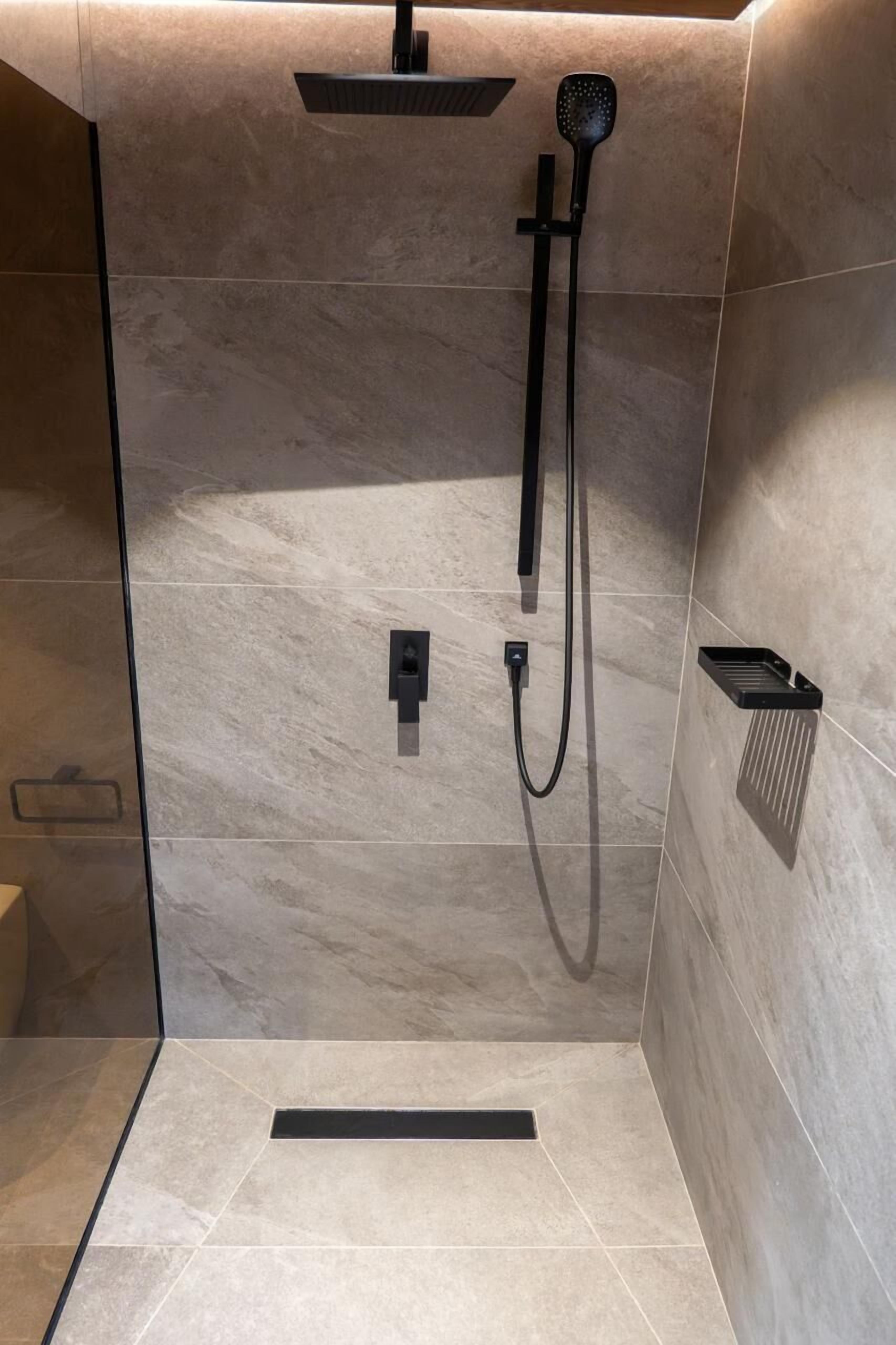 A modern shower with a handheld showerhead and a fixed overhead showerhead, a control panel, and a small shelf with a towel.