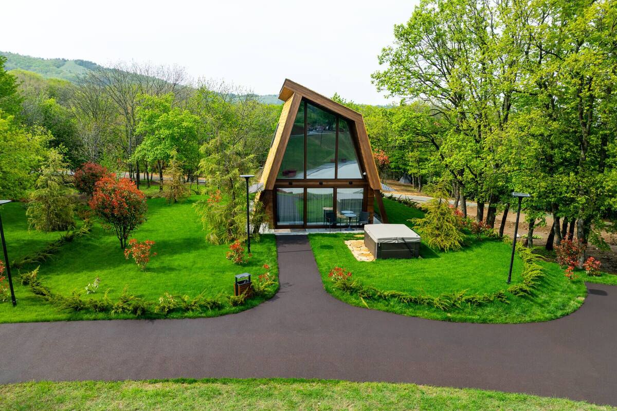 A modern building with a triangular roof, surrounded by lush greenery and a paved pathway leading to it.