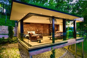 A modern glass-enclosed outdoor living area with a stone wall backdrop, furnished with leather sofas and a coffee table. - Bioli Wellness Resort (Tbilisi)