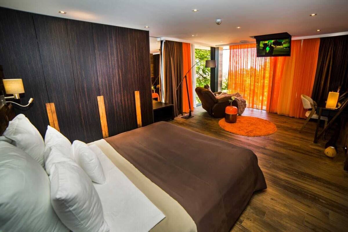 A modern hotel room with a large bed, a massage chair, a TV, and a view of the outdoors.
