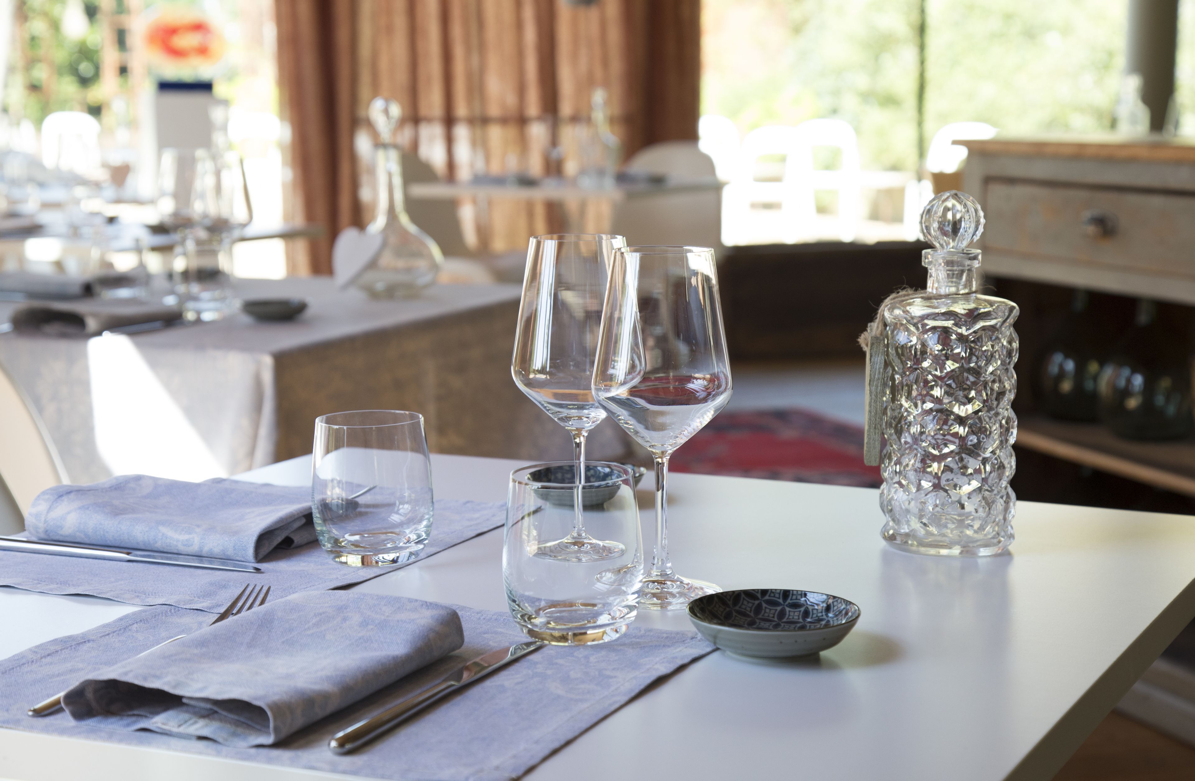 A dining table set with wine glasses, a decanter, and a bowl.