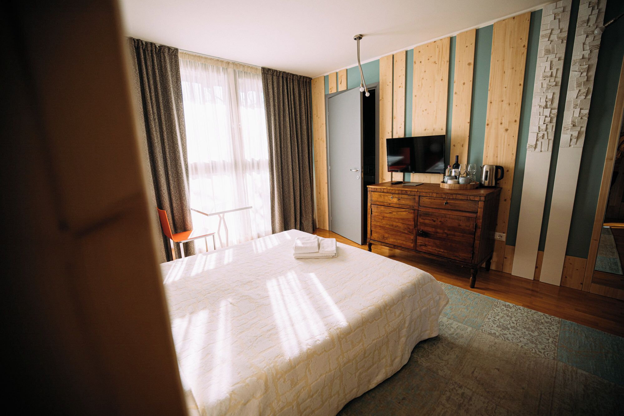 A hotel room with a bed, a wooden dresser, a television, and a window with curtains.
