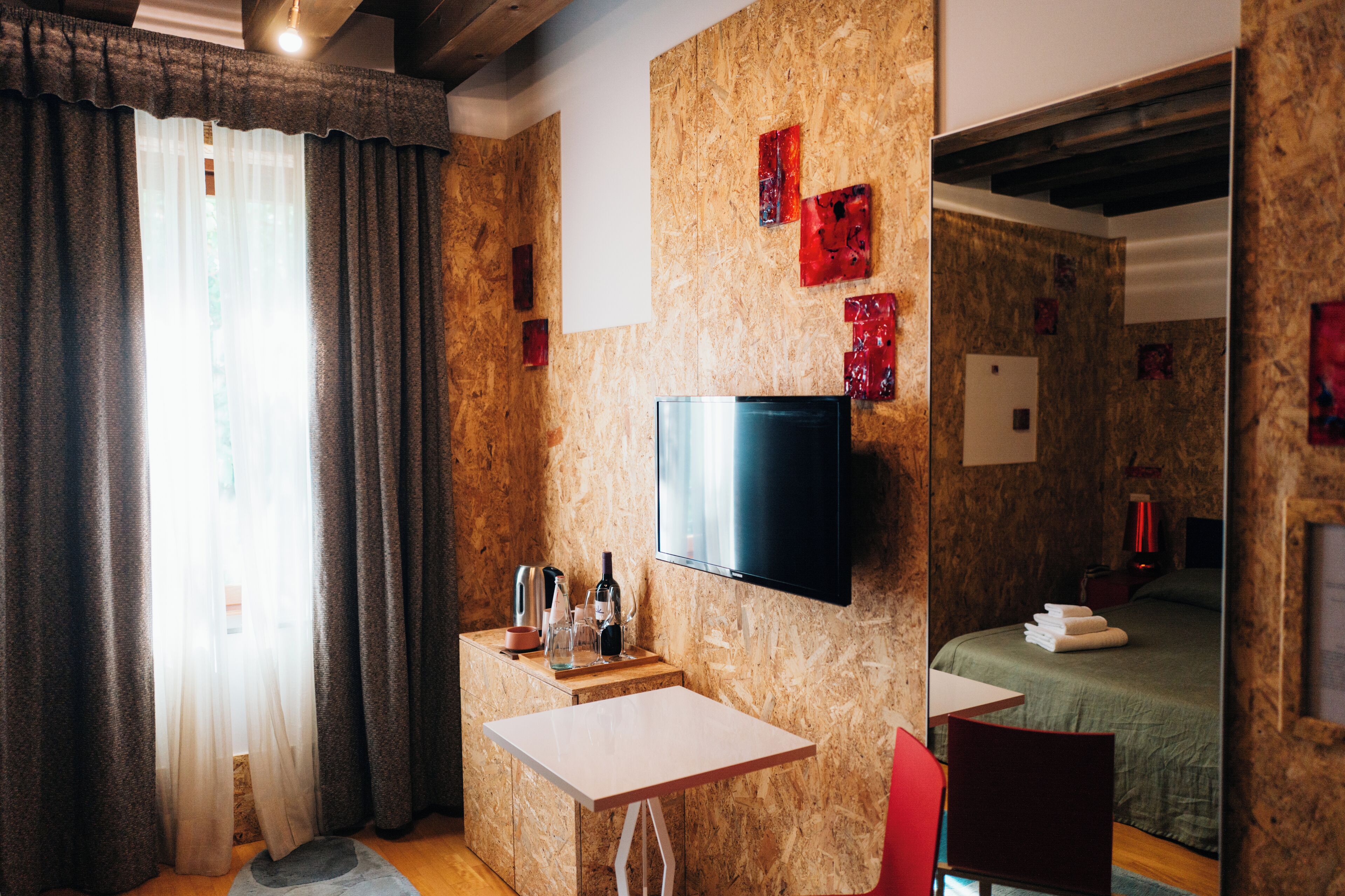 Une chambre d’hôtel avec un mur en bois, un téléviseur à écran plat, une petite table avec une chaise, un lit recouvert d’une courtepointe verte et une fenêtre avec des rideaux.