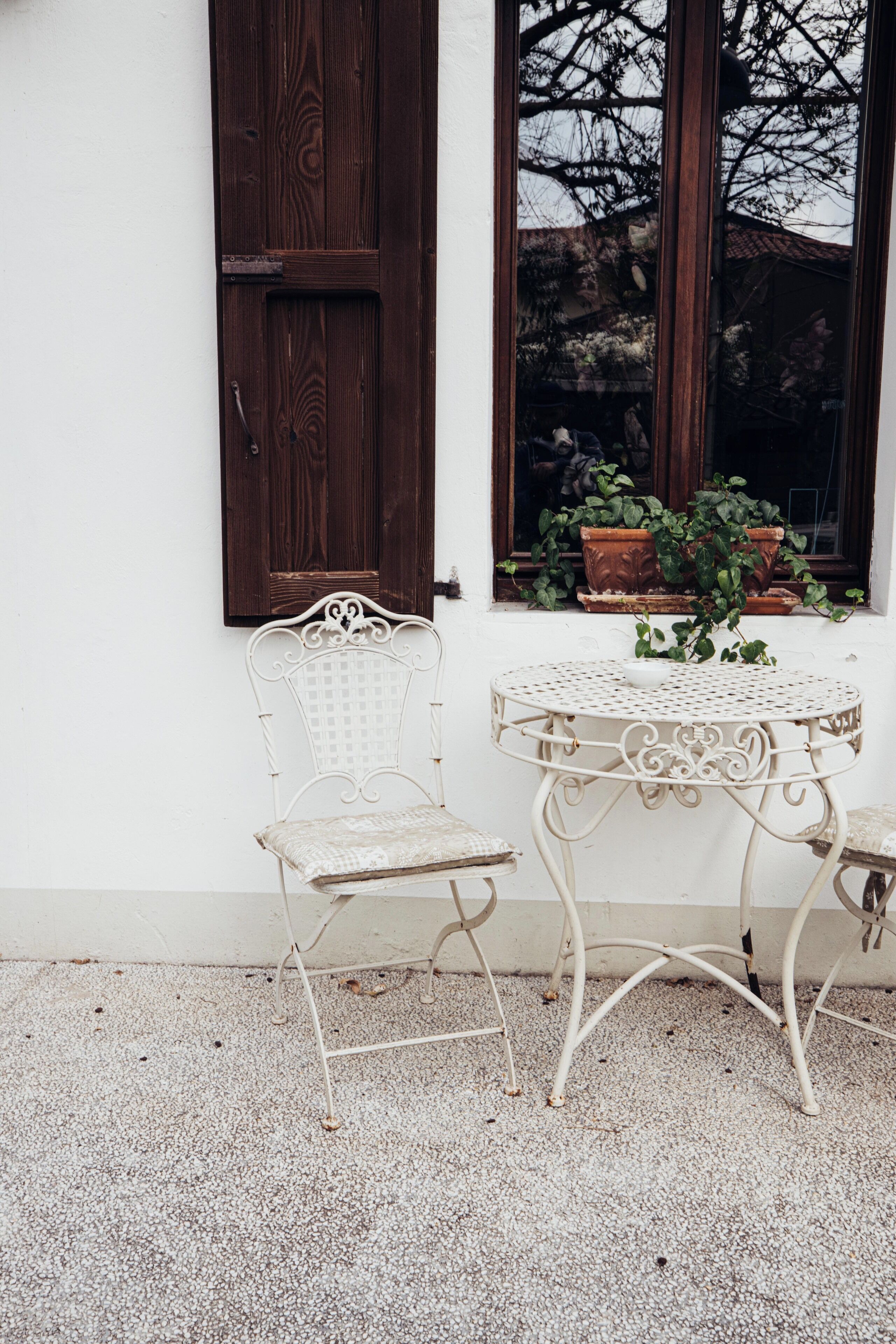 A white metal table and chair set against a white wall with a wooden door and window.