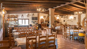 A spacious restaurant with wooden tables and chairs, a brick wall, and a television on the wall. - Cortijo Moyano (Alhama de Granada)