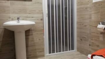 A bathroom with a white sink, a mirror, a toilet, and a shower enclosure.