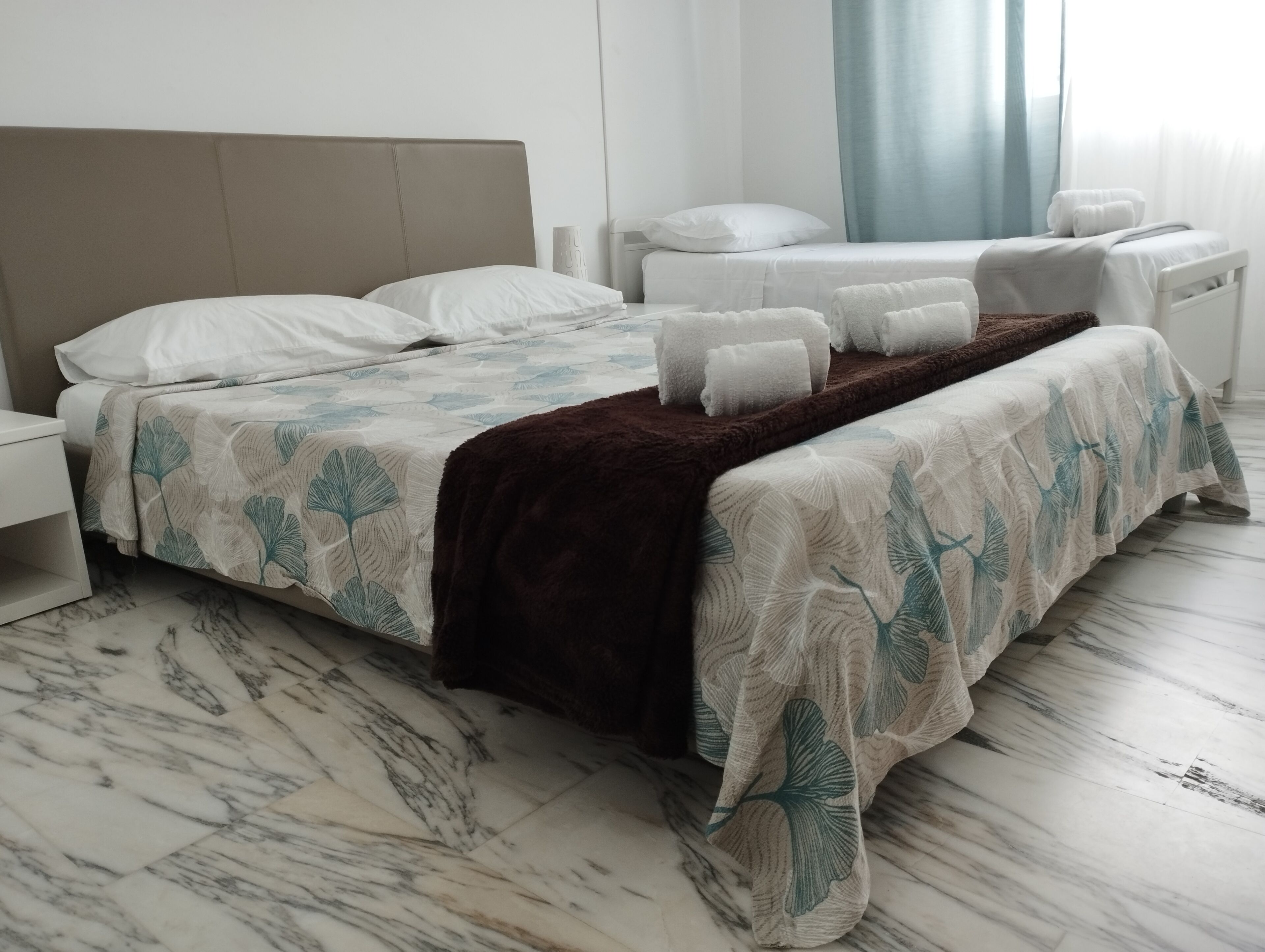 A hotel room with a large bed, a smaller bed, a nightstand, and a window with curtains.
