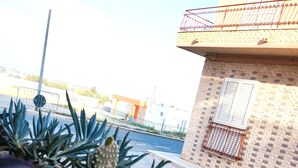 A cactus garden with a view of a building with a balcony and a fence in the background. - Thomas'home (Comiso)