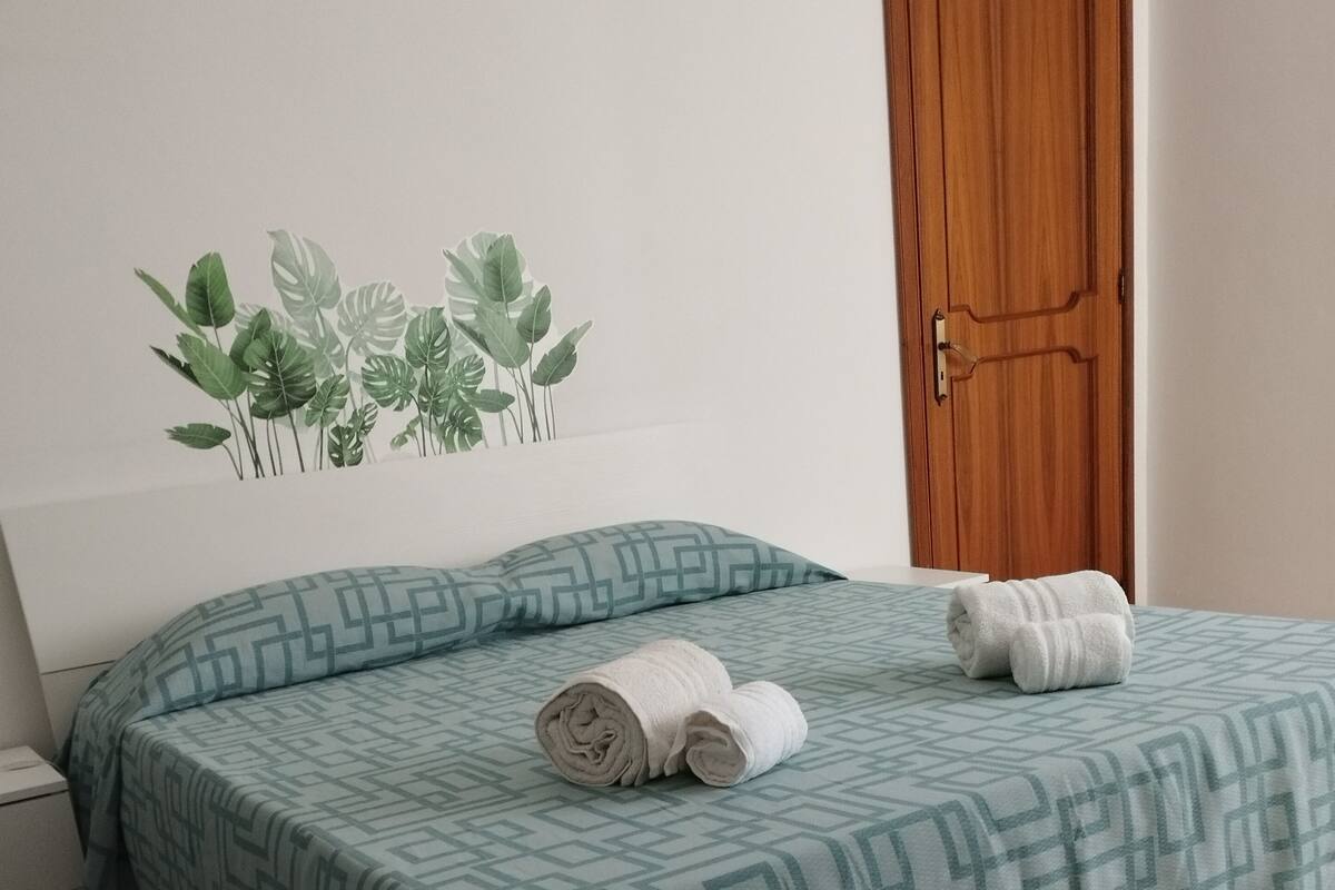 A neatly made bed with a patterned bedspread, a rolled towel, and a decorative wall sticker.