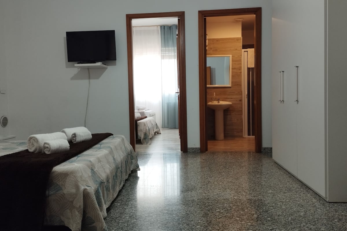 A hotel room with a bed, a TV, a bathroom with a sink and mirror, and a hallway leading to another room.