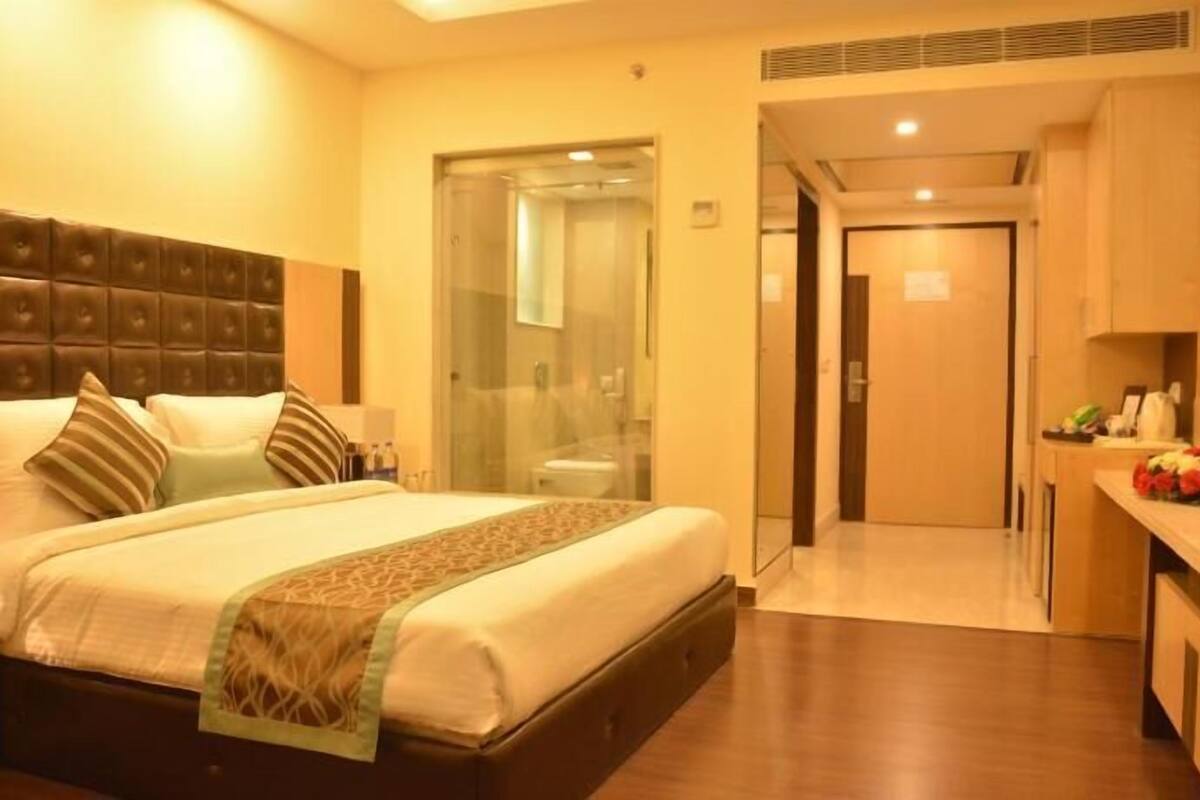 A hotel room with a bed, bedside table, and a bathroom visible through a glass door.