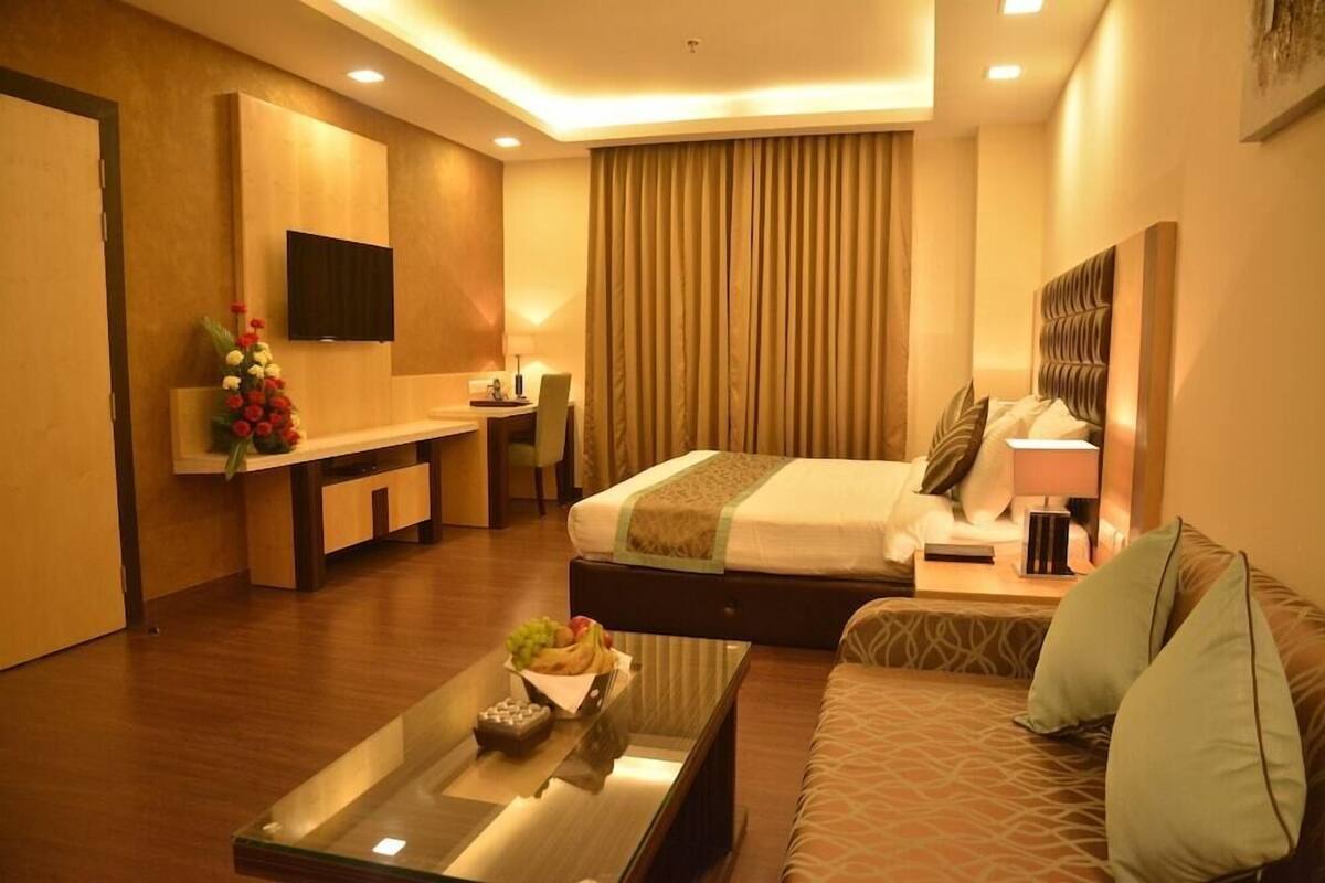 A hotel room with a bed, a sofa, a desk, and a TV.