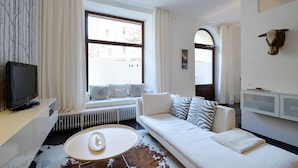 Un salon moderne avec un canapé blanc, un téléviseur et une grande fenêtre avec des rideaux.