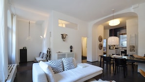 Un salon moderne avec un canapé blanc, un coin repas avec une table et des chaises, et une cuisine en arrière-plan.