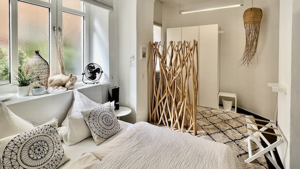 Une chambre moderne avec un grand lit, une table de chevet agrémentée d’objets décoratifs, une fenêtre avec des stores et une vue sur l’extérieur.