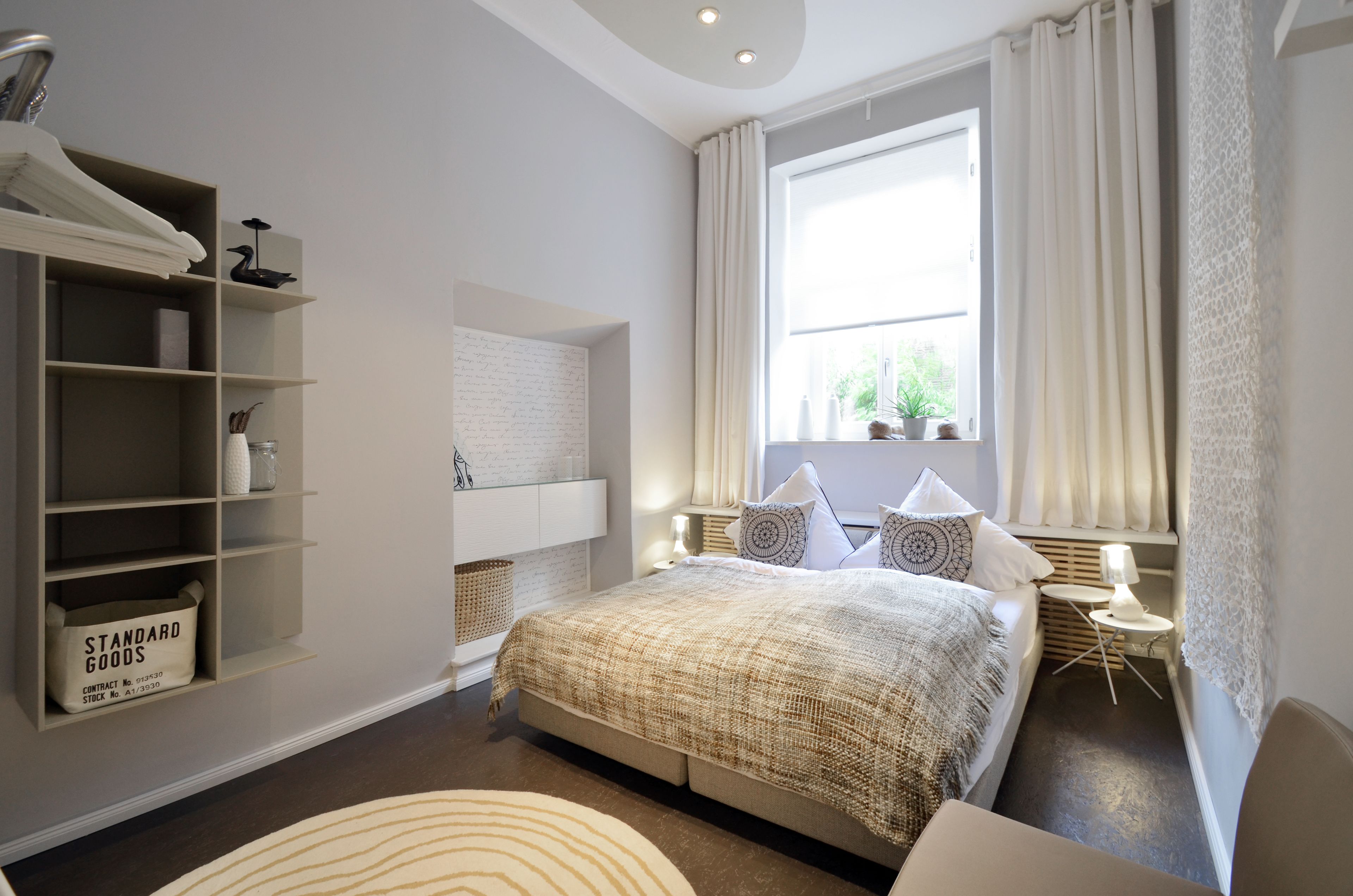 A bedroom with a large bed, a built-in wardrobe, a bedside table with a lamp, and a window with curtains.