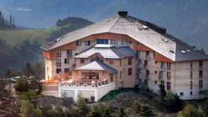 Ein großes Hotel mit mehreren Etagen, einem markanten Eingang und einer Bergkulisse im Hintergrund.